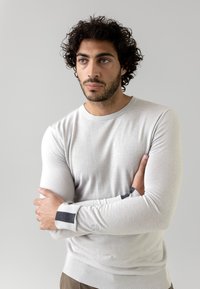 Helles graues Strickpullover mit langen Ärmeln, gerippten Bündchen mit dunklen Streifenakzenten und einem runden Halsausschnitt. Glatte, figurbetonte Textur.