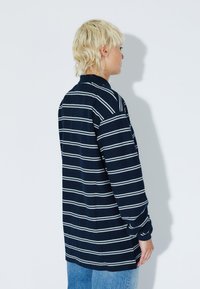 Long-sleeve navy polo shirt with white horizontal stripes, featuring a collar and relaxed fit, made from textured knit fabric.