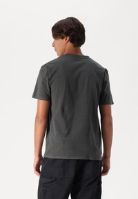 Grijze korte mouwen t-shirt, ronde hals, zachte textuur, casual pasvorm, gedragen met zwarte cargobroek, achteraanzicht.