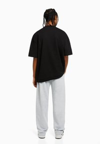 Zwarte oversized t-shirt met korte mouwen, gemaakt van katoen, gecombineerd met lichtgrijze sweatpants, met een relaxte pasvorm en elastische boorden.