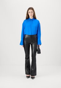 Blaues Langarmhemd mit Kragen, kombiniert mit schwarzen eng anliegenden Kunstlederhosen und schwarzen High Heels.