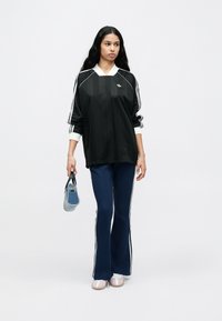 Čierny atletický top s bielymi pruhmi, doplnený o tmavomodré nohavice s bočnými pruhmi. Modelka drží modrú kabelku s textúrovaným povrchom.