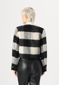 Fleece cropped jakke med et svart-hvitt rutemønster, rund hals, og detaljer med knapper på ermene. Brukt med svarte skinnbukser.