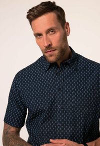 Korte mouwen marineblauw shirt met een klein bladpatroon in lichtblauw. Voorzien van knoopsluiting en een klassieke kraag. Gemaakt van lichtgewicht stof.
