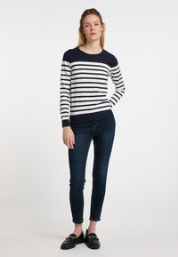 Maglione a righe blu navy e bianche con scollatura rotonda e orlo a coste, abbinato a jeans skinny blu scuro e mocassini neri.