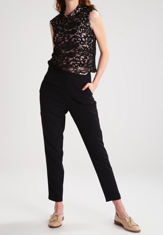 Top sin mangas de encaje negro con un cuello alto, combinado con pantalones negros tapered y mocasines beige con borlas. Texturas suaves en todo.