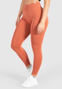 Hooggetailleerde oranje legging met een textuurafwerking, gekenmerkt door een naadloos ontwerp en gecombineerd met witte sportschoenen.