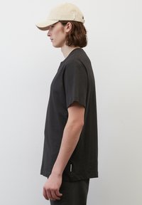 Černé bavlněné tričko má volný střih a kulatý výstřih. Světle zbarvená kšiltovka doplňuje outfit a podtrhuje ležérní styl.