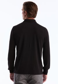 Zwarte longsleeve polo met een klassieke kraag, gladde textuur en een aansluitend ontwerp, gecombineerd met lichtgrijze broeken.