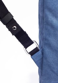 Borsa di tessuto blu con superficie texturizzata, dotata di una tracolla nera fissata da una fibbia in metallo argentato e un dettaglio in pelle.