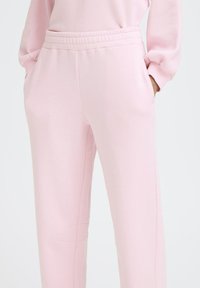 Roza trenirke iz mehkega materiala, z raztegljivim pasom, stranskimi žepi in udobnim krojem ter gladko teksturo.