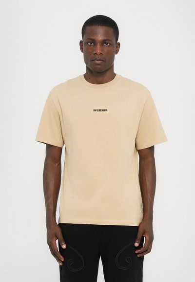 T-shirt en coton beige à manches courtes, avec un col rond et un petit logo imprimé en noir sur la poitrine. Design simple et sans embellissement.