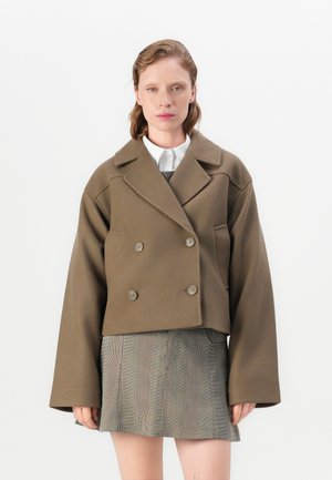 Veste cropped à double boutonnage en laine mélangée vert olive avec de gros boutons et des manches larges, associée à une jupe à carreaux grise.