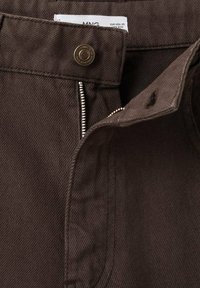 Pantalon en denim marron avec une fermeture éclair et bouton, présentant une texture en côtes diagonales et des coutures contrastantes le long des seams.