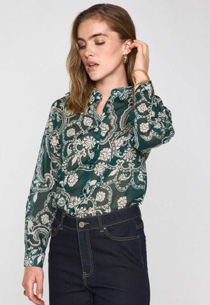 Grün gemustertes Hemd mit Blumenprint und langen Ärmeln, kombiniert mit dunkler Jeans. Glattes Material, Kragen und Manschetten sichtbar.