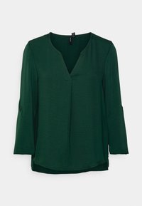Mörkgrön blus med lång ärm och V-ringning samt knappar på ärmarna, uppvisad mot en vit bakgrund.