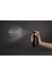 Schwarze Sprühflasche in der Hand gehalten, mit fein vernebelnder Düse, und weißem Text auf dem Etikett. Der Hintergrund ist dunkelgrau und hebt das Produkt hervor.
