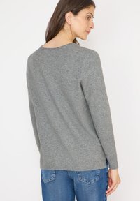 Grauer Pullover mit rundem Halsausschnitt, langen Ärmeln und geripptem Saum. Weiche Textur, lässige Passform und glatte Oberfläche.