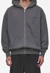 Grå ziphoodie gjord av mjukt tyg, med en känguruficka, ribbad mudd och nederkant, samt en liten logotyp på bröstet.