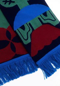 Dzianinowy szalik z wyrazistymi wzorami w kolorach czerwonym, niebieskim, zielonym i granatowym. Teksturowana tkanina z niebieskimi frędzlami na końcach.