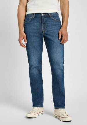 Dunkelblaue Denim-Jeans mit geradem Schnitt, Fünf-Taschen-Design und subtiler, ausgewaschener Textur, kombiniert mit weißen Sneakers im Low-Top-Stil.