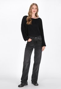 Pulover negru din tricot cu mâneci largi, asociat cu blugi negri cu talie înaltă. Ținuta are o croială lejeră și detalii de textură subtile.