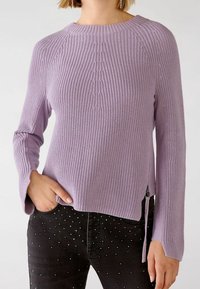 Lilac knitted sweater featuring a ribbed texture, round neckline, flared sleeves, and side zip detail. Paired with black studded jeans.