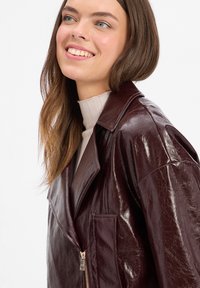 Giacca in ecopelle bordeaux con finitura lucida, collo oversize e chiusura con zip. Presenta una tasca frontale e una texture liscia.