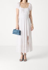 Vit, lång maxiklänning med puffärmar och en resår i midjan, med en slits framtill. Kombinerad med en blå clutch och blå klackskor.