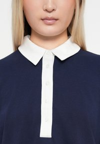 Námornícky polo tričko s bielym golierom a zapínaním na gombíky; má hladkú textúru a klasický dizajn.