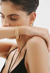 Pulseras de oro con texturas variadas llevadas en un brazo desnudo, mostrando un diseño elegante sobre un atuendo negro.