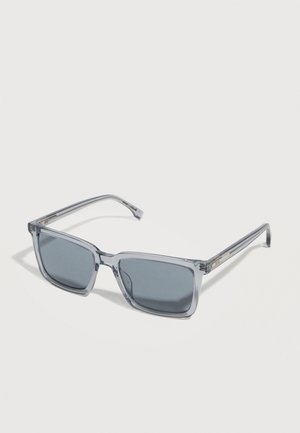 Prostokątne okulary przeciwsłoneczne z szarawym odcieniem, z przezroczystymi szarymi plastikowymi oprawkami i cienkimi zausznikami, pokazane na białej powierzchni.