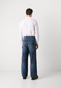 Modre denimske cargo hlače ohlapnega kroja, z več žepi in značko na hrbtni strani. V kombinaciji z belo srajco s klasičnim ovratnikom.