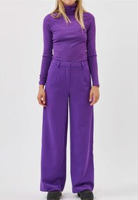 Col roulé côtelé violet et pantalon violet à jambes larges. Le pantalon présente une taille haute et une coupe ajustée, avec un tissu lisse et des plis à l'avant.