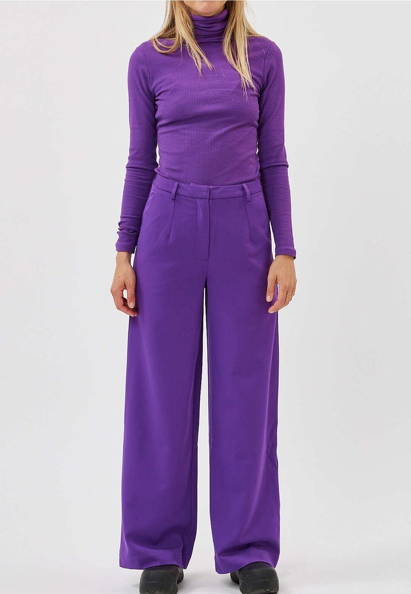 Col roulé côtelé violet et pantalon violet à jambes larges. Le pantalon présente une taille haute et une coupe ajustée, avec un tissu lisse et des plis à l'avant.