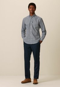 Blau-weißer karierter Hemd mit Knöpfen, aus Baumwolle, mit Kragen. Kombiniert mit navyblauen Hosen und braunen Wildlederschuhen. Einfaches Design, körperbetonter Schnitt.