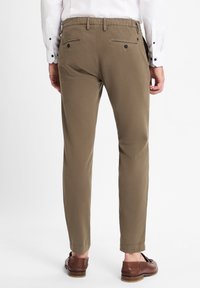 Beige chinos with a slim fit, elastic waistband, and two back pockets. Worn with brown leather shoes. Smooth cotton fabric.