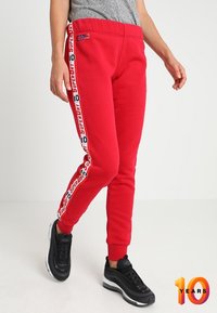 Rode joggerbroeken van zacht materiaal, met witte zijstrepen met "Superdry" branding en een aangesloten boord. Draag ze met zwarte sneakers.