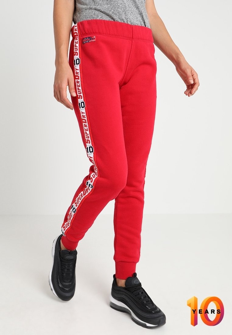 Rode joggerbroeken van zacht materiaal, met witte zijstrepen met "Superdry" branding en een aangesloten boord. Draag ze met zwarte sneakers.