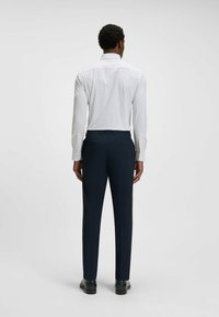 Witte shirt met kleine zwarte stippen, gecombineerd met donkerblauwe broek. Het shirt heeft lange mouwen en een standaard kraag. Soepele, getailleerde fit.