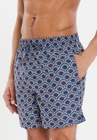 Pantaloni da nuoto con un motivo geometrico blu e forme esagonali in arancione e bianco, vita elastica con cordoncino, tasche laterali.