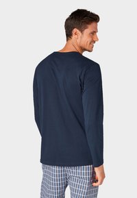 Marineblauw langemouwen shirt van zachte stof, met een ronde hals en een casual pasvorm, gedragen met geruite pyjamabroek.
