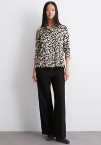 Ein leopardgemustertes Hemd in Beige und Schwarz, kombiniert mit hoch taillierten schwarzen Hosen und schwarzen Schuhen, mit langen Ärmeln.