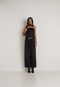 Top strapless de cetim preto, calças de ganga pretas largas de cintura alta e botins pretos, com uma cintura acentuada e textura lisa.