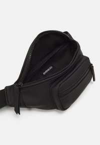 Sac bandoulière noir en tissu lisse. Comprend un compartiment principal zippé et une petite poche frontale zippée. Design compact et élégant.
