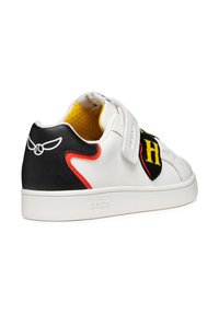Witte sneaker met zwarte en rode accenten, klittenbandsluitingen en een geborduurd patch met een letter. Textuur rubberen zool en mesh voering.
