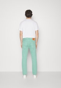 Mintgröna jeans med rak passform, bakfickor och en distinkt logotyp i orange läder. Bärs med en enfärgad vit t-shirt.