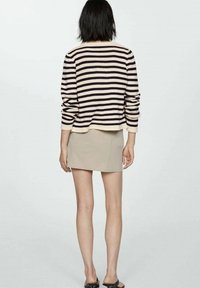 Maglione a righe in crema e blu navy, abbinato a una mini gonna beige. Il maglione ha una vestibilità comoda e maniche lunghe con polsini a coste.