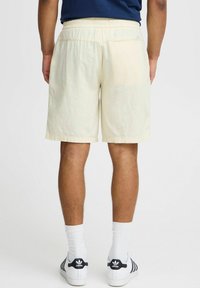Licht beige shorts met een elastische tailleband, zijzakken en een comfortabele pasvorm, gecombineerd met witte sokken en sneakers met zwarte accenten.