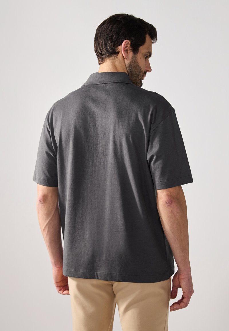 Polo shirt da uomo grigio scuro con vestibilità rilassata, maniche corte e colletto classico, realizzato in morbido cotone.